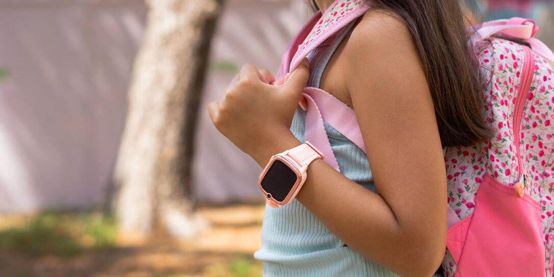 Elementary age girl wearing smartwatch and carrying backpack at park