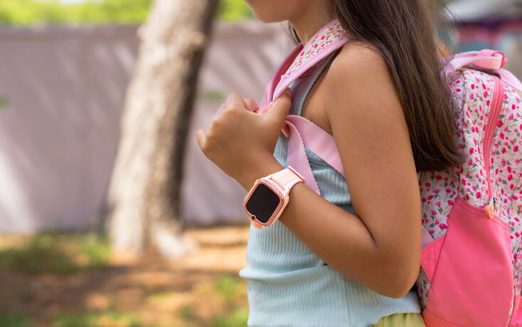 Elementary age girl wearing smartwatch and carrying backpack at park