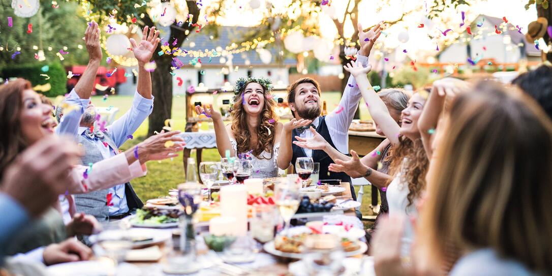 Bride and groom with guests at wedding reception outside in the backyard.