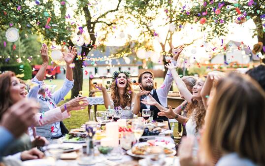 Bride and groom with guests at wedding reception outside in the backyard.