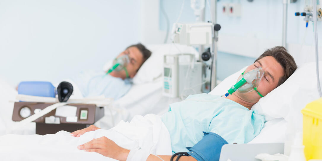 Two patients in hospital beds wearing oxygen masks