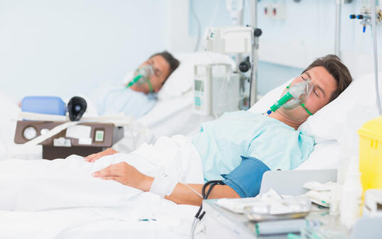 Two patients in hospital beds wearing oxygen masks