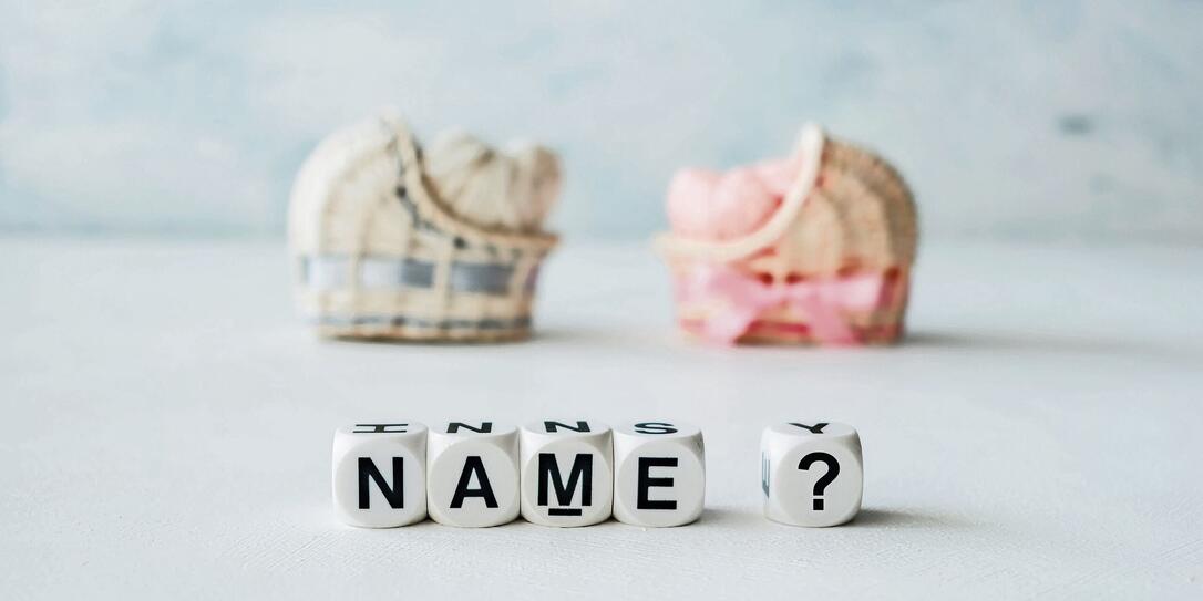 Concept of choosing baby name. Pink and blue decorative straw cradles with thread hearts and text name? on light background Concept of choosing baby name. Pink and blue decorative straw cradles with thread hearts and text name? on light background