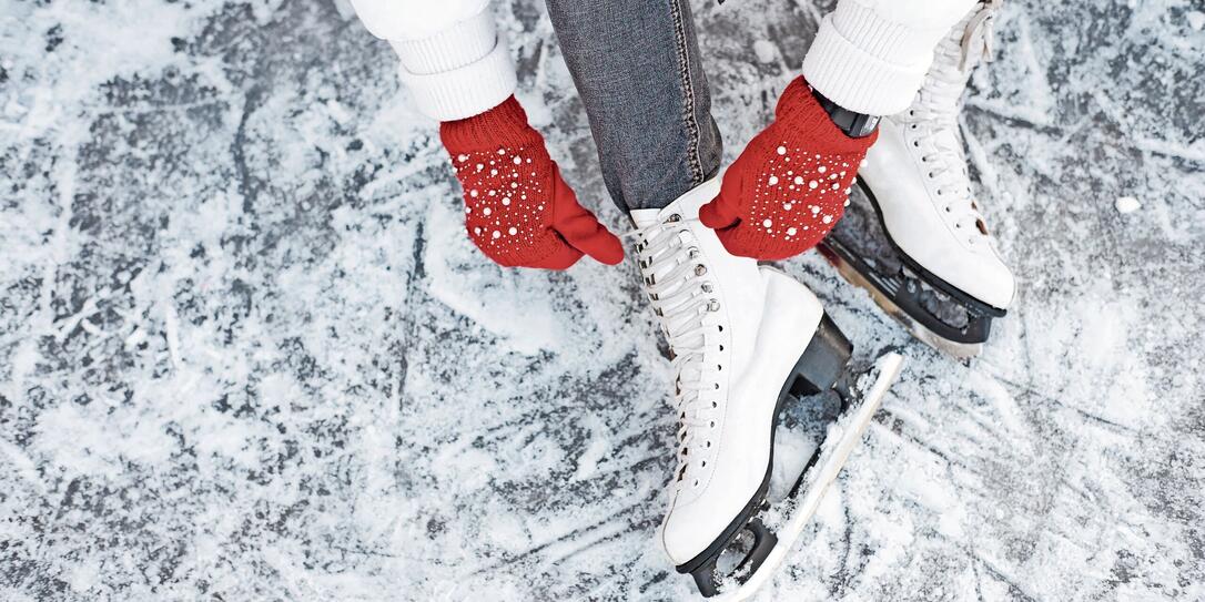 Girl tying shoelaces on ice skates before skating on the ice rink, hands in red knitted gloves. Girl tying shoelaces on ice skates before skating on the ice rink, hands in red knitted gloves.