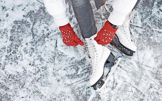 Girl tying shoelaces on ice skates before skating on the ice rink, hands in red knitted gloves.