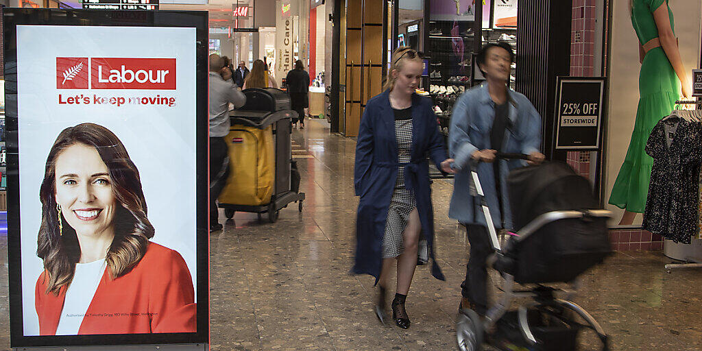 Menschen gehen in einem Einkaufszentrum an einer elektronischen Plakatwand vorbei, die ein Foto der neuseeländischen Premierministerin Jacinda Ardern zeigt. Neuseeländer gehen bei den Parlamentswahlen am Samstag, den 17.10.2020, an die Urnen. Foto: Mark Baker/AP/dpa