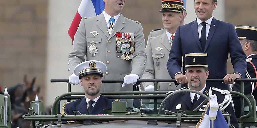 Emmanuel Macron (r), Präsident von Frankreich, und der Generalstabschef der französischen Armeen, General Francois Lecointre stehen im Kommandowagen, während der Militärparade zum französischen Nationalfeiertag. Foto: Christophe Ena/AP/dpa