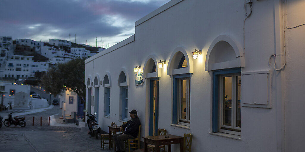 Ein Mann sitzt allein auf einem Stuhl vor einem Restaurant auf der Insel Astypalea. Foto: Petros Giannakouris/AP/dpa
