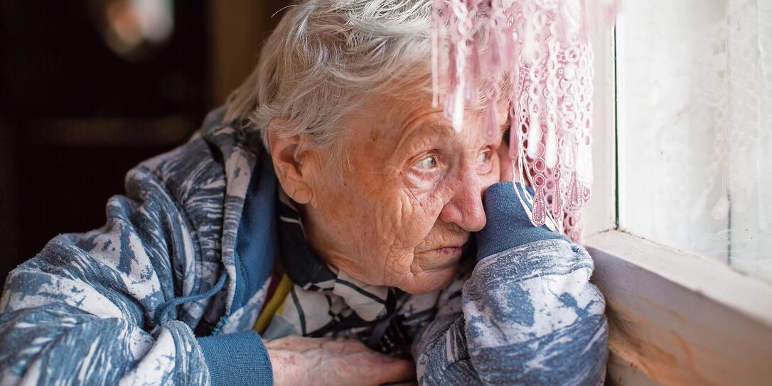 Elderly woman sadly looking out the window.