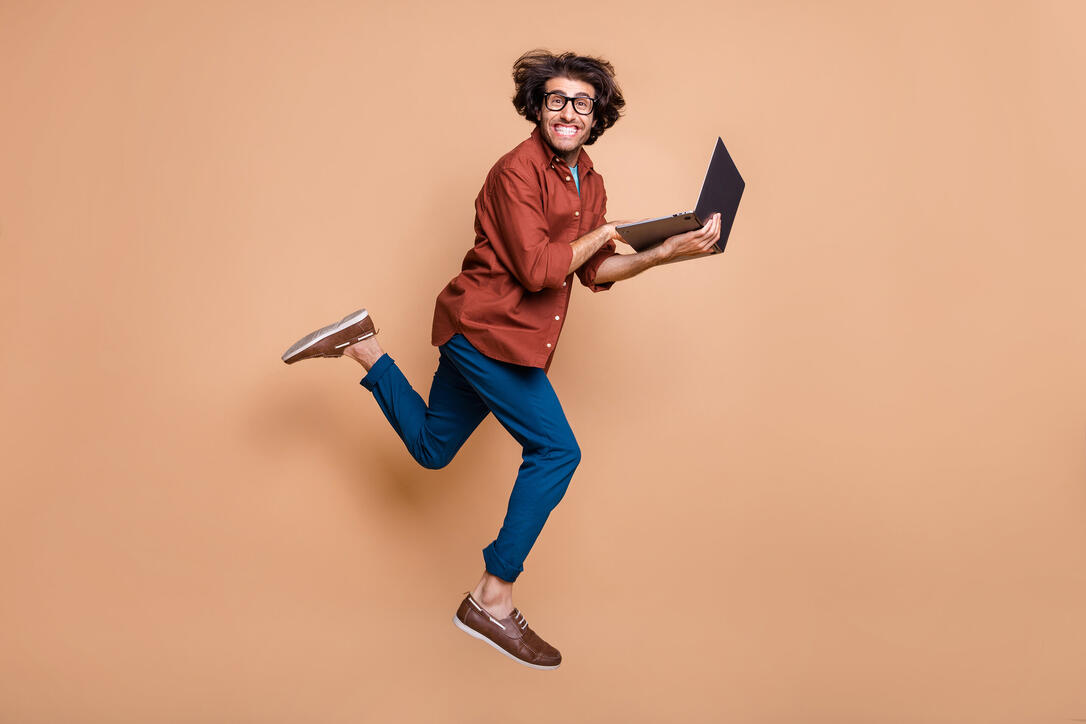Full length photo portrait of man running holding laptop jumping up isolated on pastel beige colored background