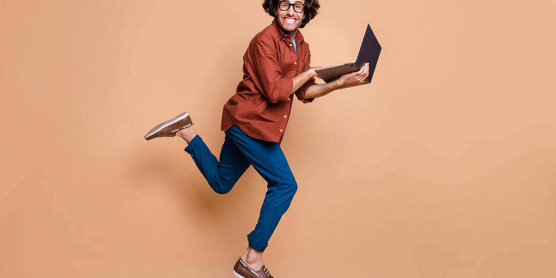 Full length photo portrait of man running holding laptop jumping up isolated on pastel beige colored background