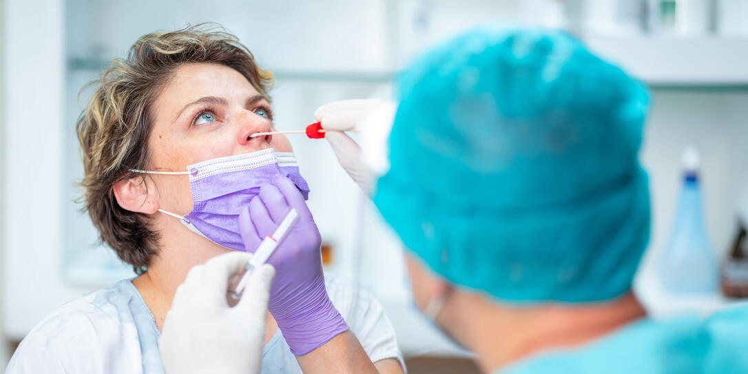 Doctor taking nasal swab from female patient with face mask