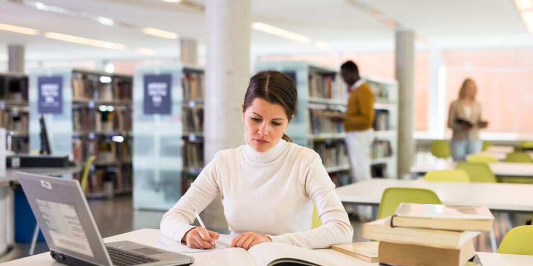 Portrait of smiling woman with laptop and book in public library