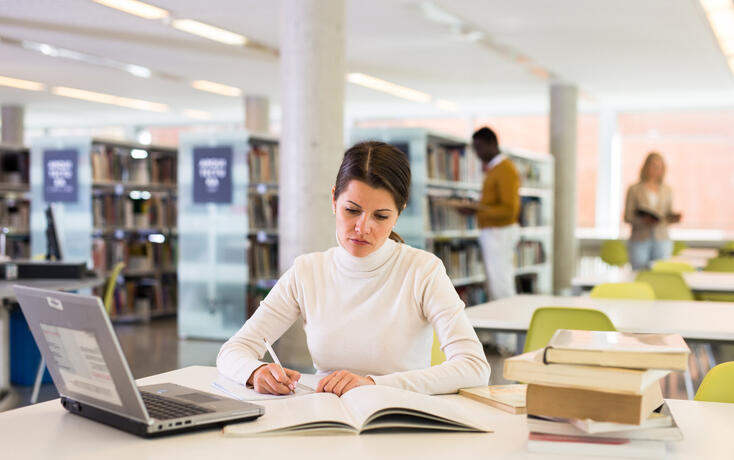 Portrait of smiling woman with laptop and book in public library