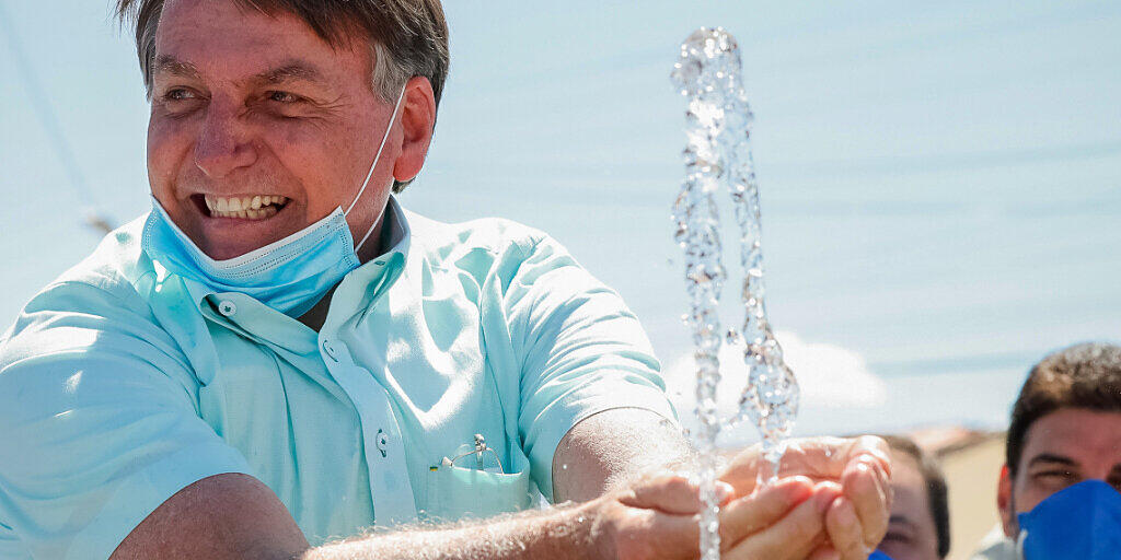 HANDOUT - Auf diesem vom brasilianischen Präsidentenamt zur Verfügung gestellten Bild lächelt Jair Bolsonaro, Präsident von Brasilien, mit untergezogenem Mundschutz, während er an einem Brunnen zur lokalen Wasserversorgung mit Wasser spielt. Foto: Alan Santos/Palacio Planalto/dpa