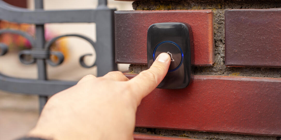 Hand Pressing Doorbell on Red Brick Wall