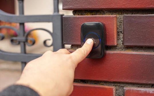 Hand Pressing Doorbell on Red Brick Wall