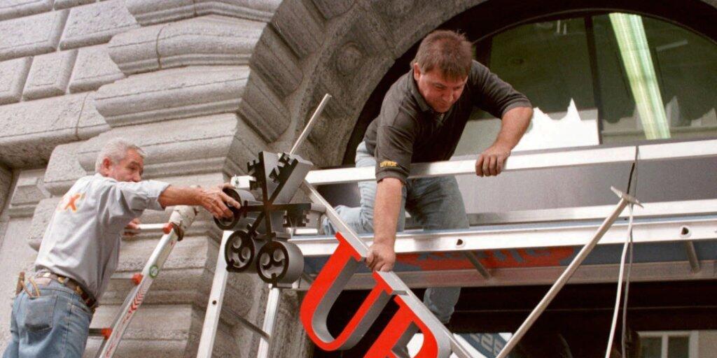 Handwerker hängen im Juni 1998 nach der genehmigten Fusion zwischen der früheren Schweizerischen Bankgesellschaft und des Schweizerischen Bankvereins die neuen UBS-Schilder auf. (Archiv)