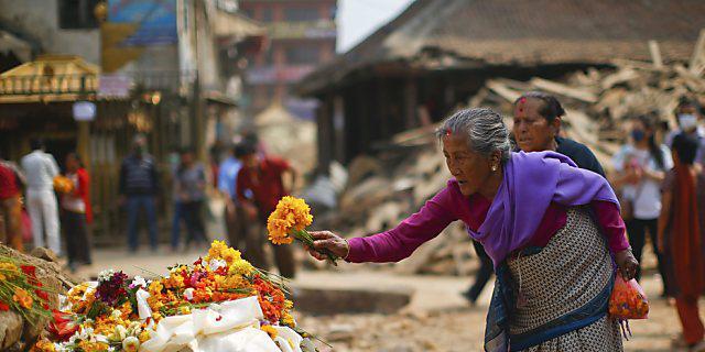 Eine alte Nepalesin legt Blumen auf die Haustrümmer Eine alte Nepalesin legt Blumen auf die Haustrümmer