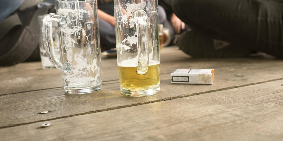 Friends Sitting By Beer Glass And Cigarette Pack On Boardwalk