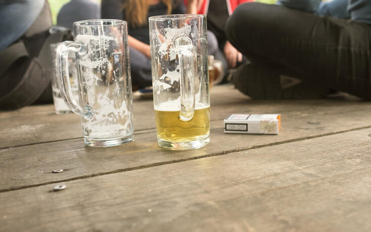 Friends Sitting By Beer Glass And Cigarette Pack On Boardwalk