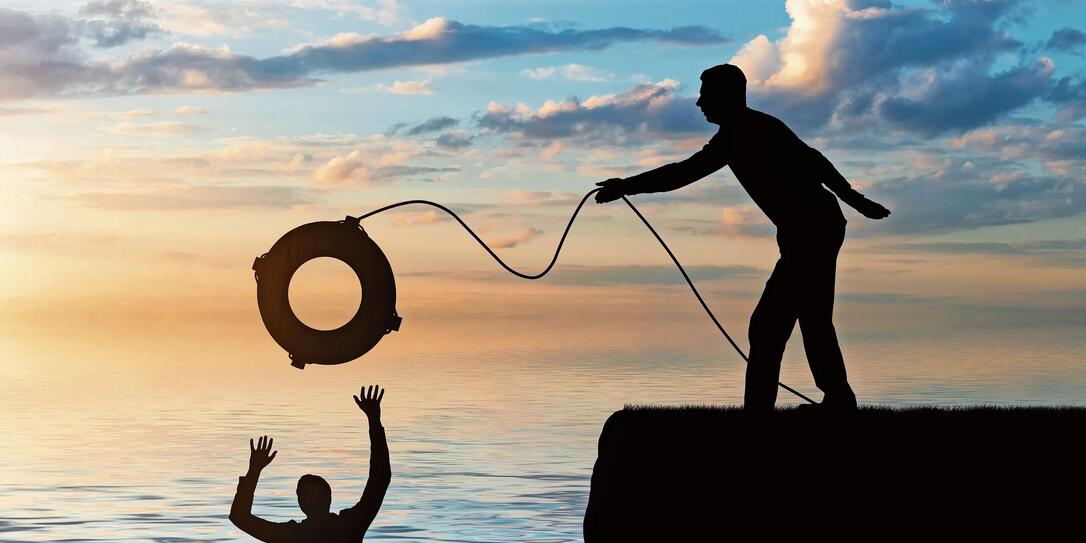 A silhouette of a man throws a lifeline to another man who is drowning in the water