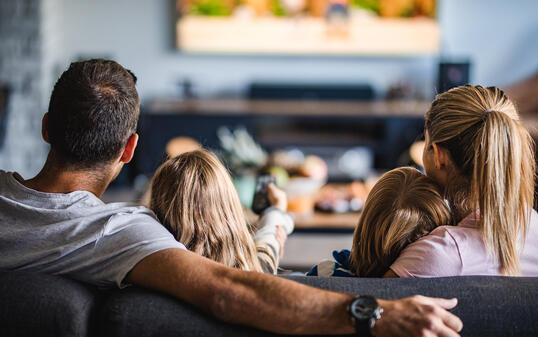 Rear view of a family watching TV on sofa at home.