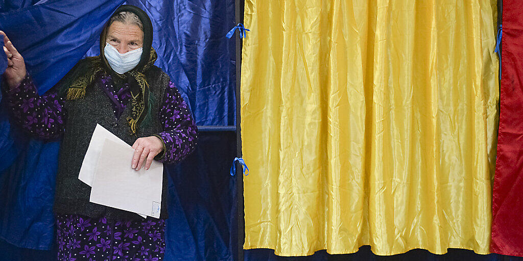 Eine Frau mit Mund-Nasen-Schutz verlässt eine Wahlkabine, nachdem sie bei den Parlamentswahlen ihre Wahlstimme abgegeben hat. Foto: Alexandru Dobre/AP/dpa