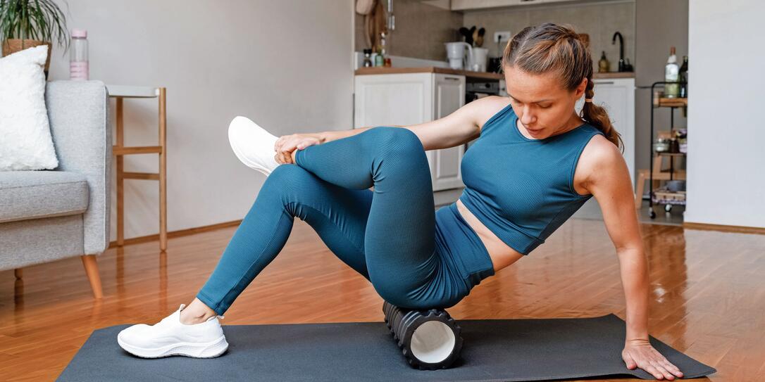 Athletic woman does a workout at home, using a foam roller to release leg muscles. Self-myofascial release.