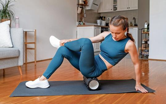 Athletic woman does a workout at home, using a foam roller to release leg muscles. Self-myofascial release.