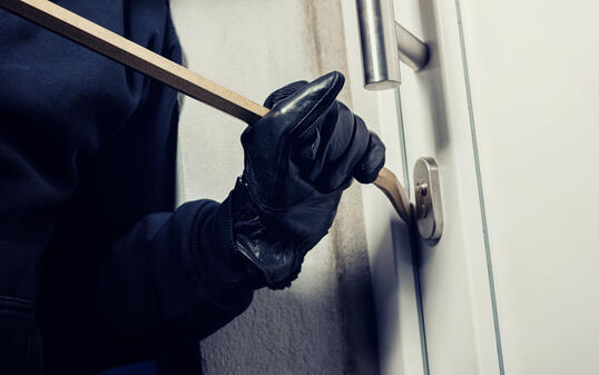 burglar using crowbar to break a home door at night