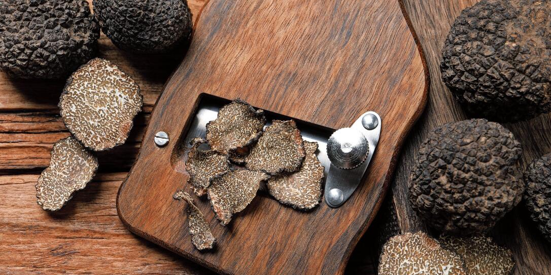 Shaver with whole and sliced black truffles on wooden table, flat lay
