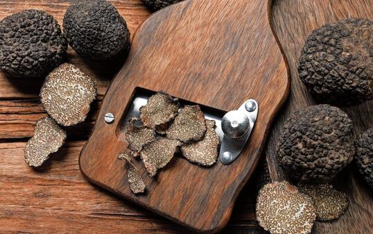 Shaver with whole and sliced black truffles on wooden table, flat lay