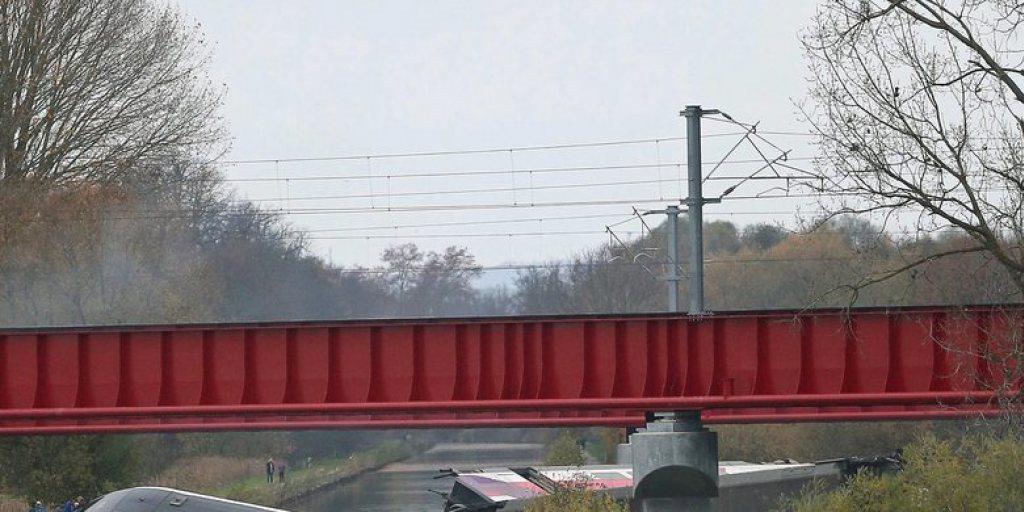 Der Zug entgleiste mit hoher Geschwindigkeit. Die Wagen liegen zerstreut auf einem Feld und in einem Kanal.