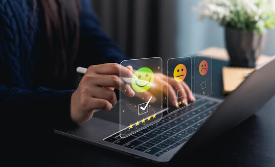 Close-up hand woman interacts with a laptop to express feedback using emotion icons and star ratings, reflecting the importance of customer satisfaction digital workplace.