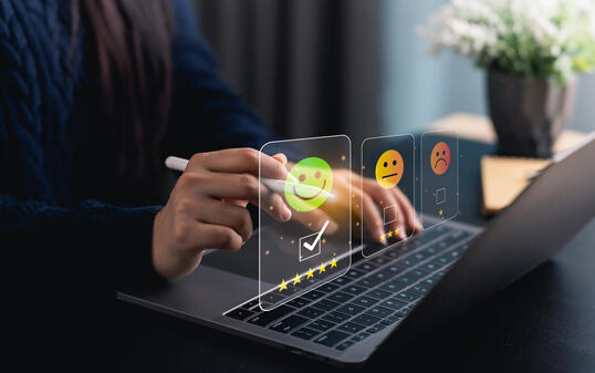 Close-up hand woman interacts with a laptop to express feedback using emotion icons and star ratings, reflecting the importance of customer satisfaction digital workplace.