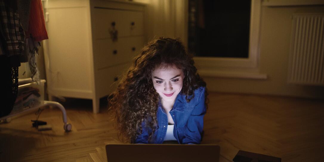 Woman sitting lying on the floor and working on laptop at night.