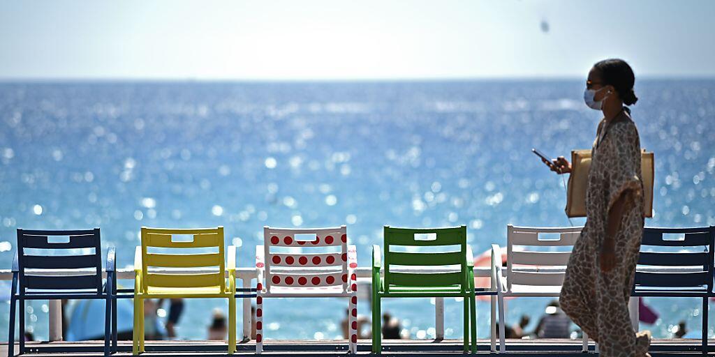 Eine Frau geht auf der Strandpromenade an der französischen Riviera an Stühlen vorbei. Foto: Anne-Christine Poujoulat/AFP/dpa