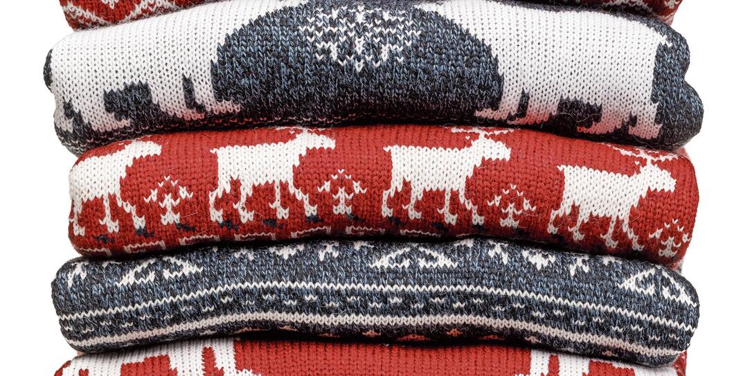 Stack of folded knitted Christmas turtleneck sweaters on white background
