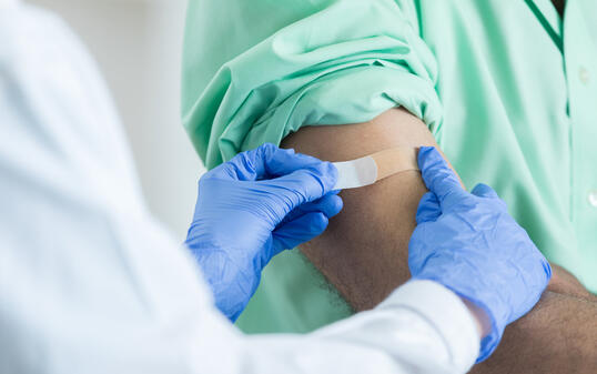 Closeup of unrecognizable pharmacist placing bandaid on customer's arm