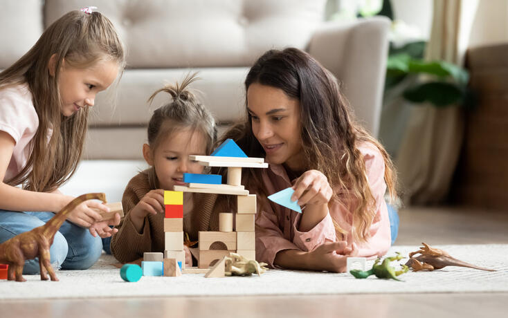 Mother play wooden blocks with two little daughters at home