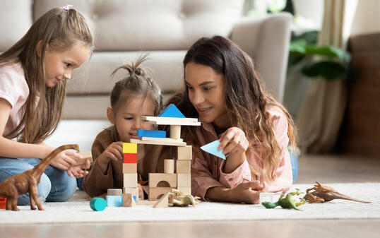 Mother play wooden blocks with two little daughters at home