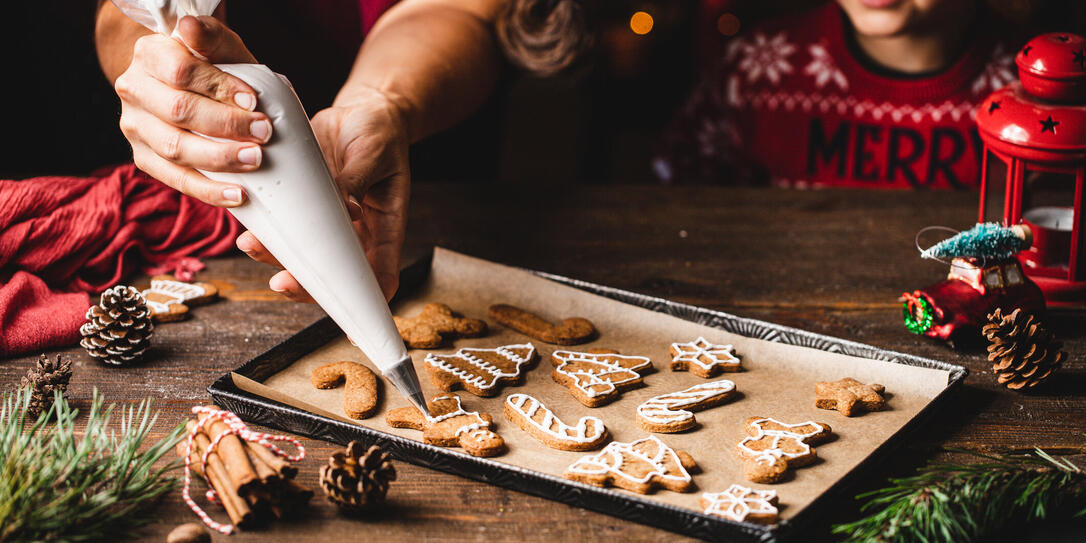 Woman icing gingerbread christmas cookie by son in kitchen