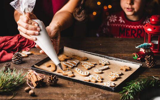 Woman icing gingerbread christmas cookie by son in kitchen