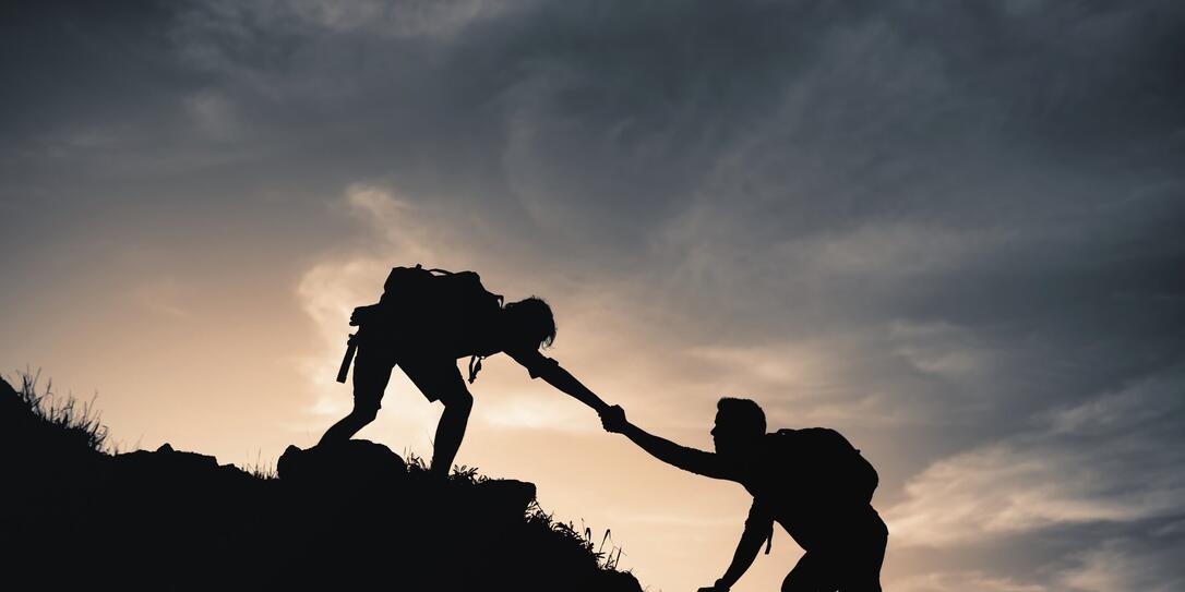 Mountain climber helping fellow climber up rocky edge of a mountain cliff.