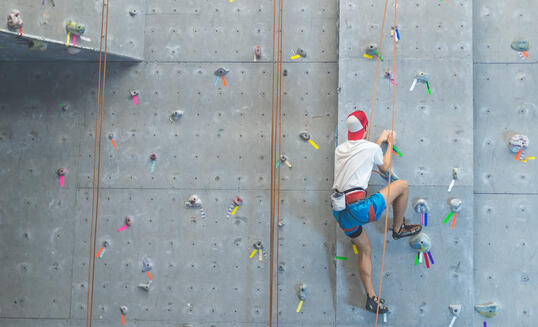 College student scaling indoor climbing wall