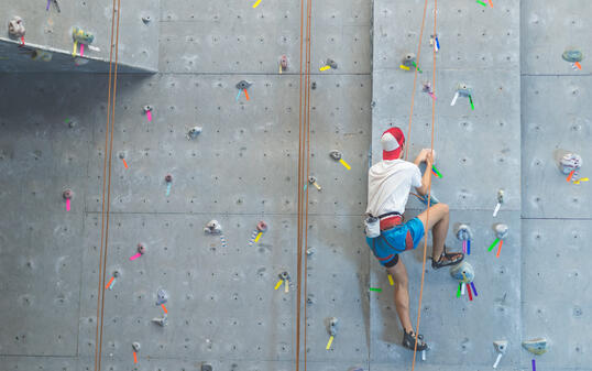 College student scaling indoor climbing wall