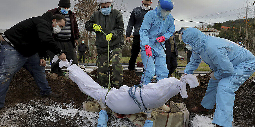 dpatopbilder - Freiwillige und Angehörige, die Schutzkleidung und Masken tragen, senken den Leichnam eines Mannes, der am Coronavirus gestorben ist, in ein Grab auf einem Friedhof am Rande der Stadt Ghaemshahr. Foto: Ebrahim Noroozi/AP/dpa dpatopbilder - Freiwillige und Angehörige, die Schutzkleidung und Masken tragen, senken den Leichnam eines Mannes, der am Coronavirus gestorben ist, in ein Grab auf einem Friedhof am Rande der Stadt Ghaemshahr. Foto: Ebrahim Noroozi/AP/dpa