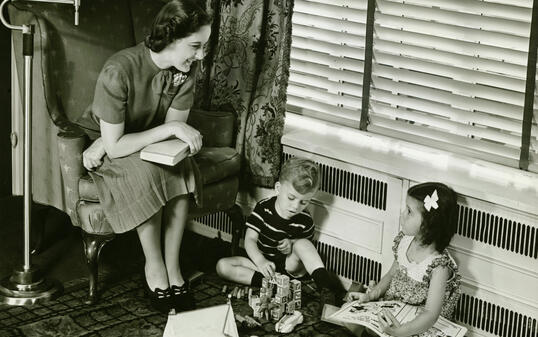 Mother watching over son and daughter (4-5) playing in living room, (B&W)