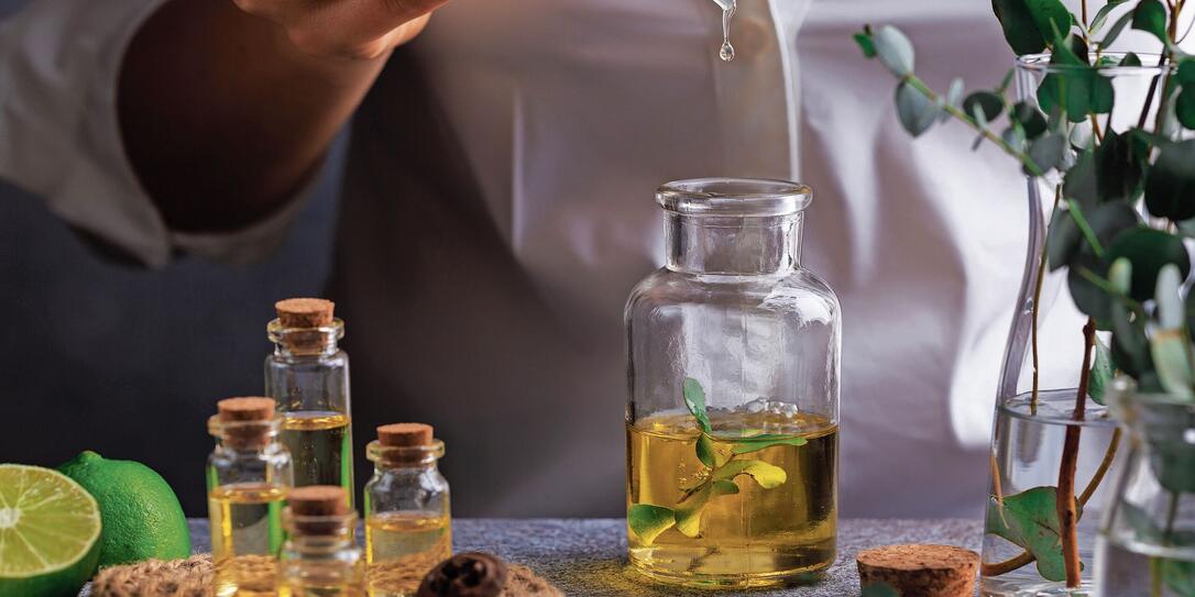 Woman hand pouring eucalyptus essential oil into bottle on grey table